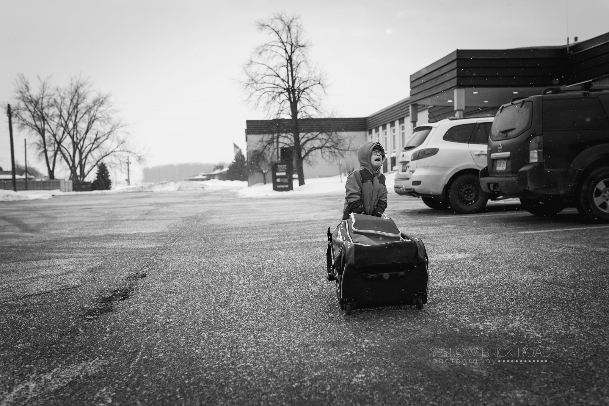 black and white lifestyle image of young boy trying to pull hockey bag in st.jacobs