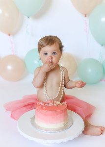 brunette baby testing birthday cake in pearls