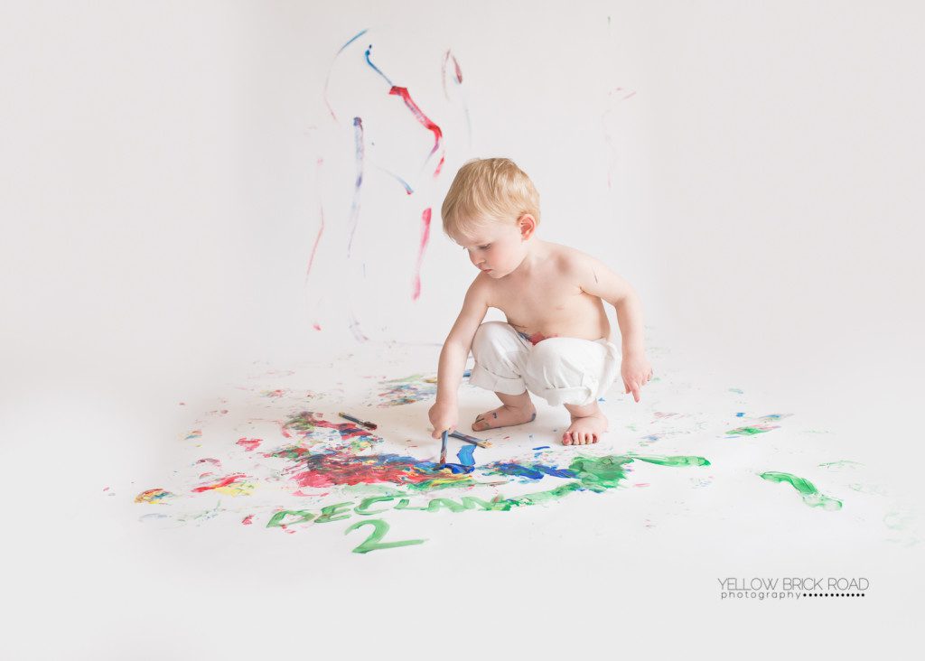 blonde little boy painting on white backdrop
