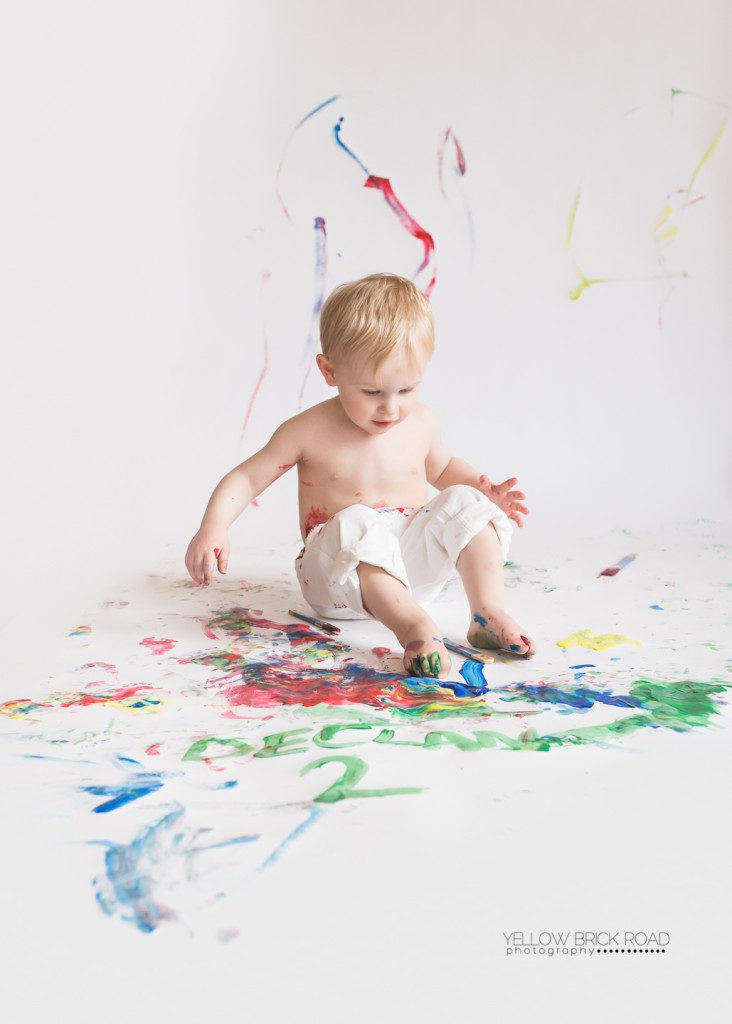 little blonde boy rubbing his feet in the paint during his paint smash session