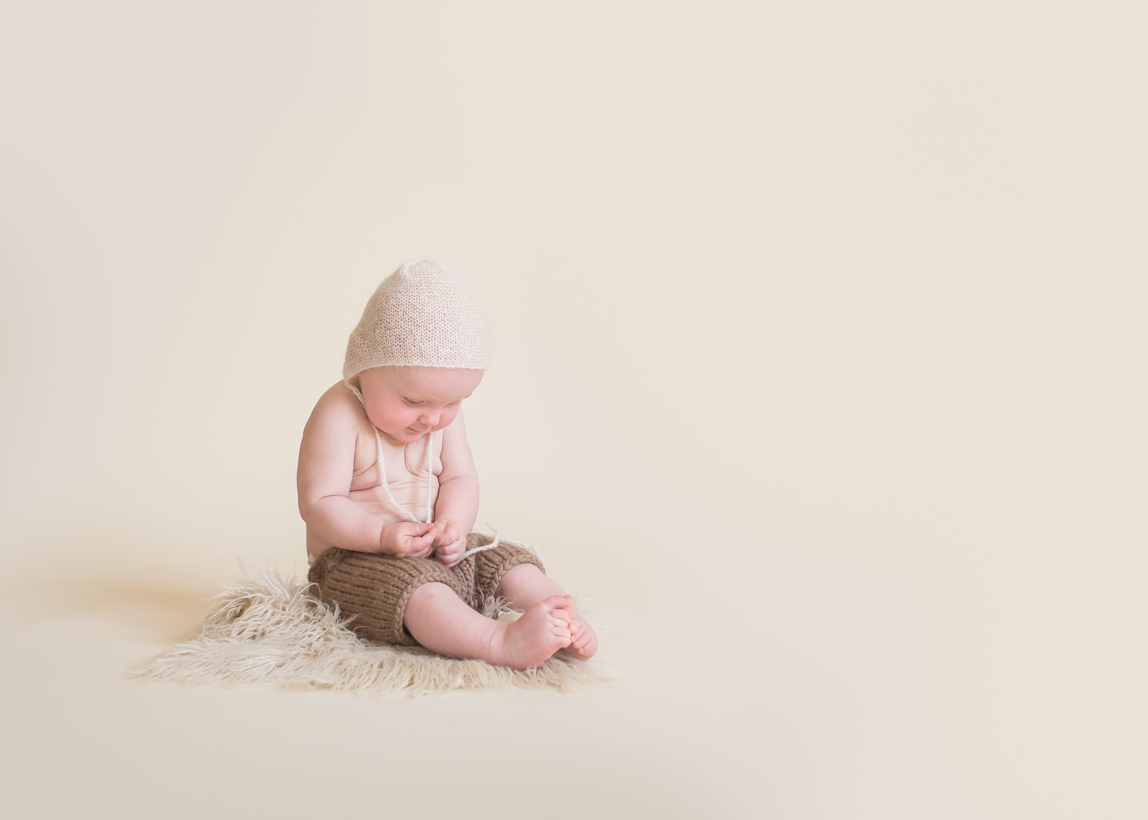 baby boy in bonnet on cream backdrop