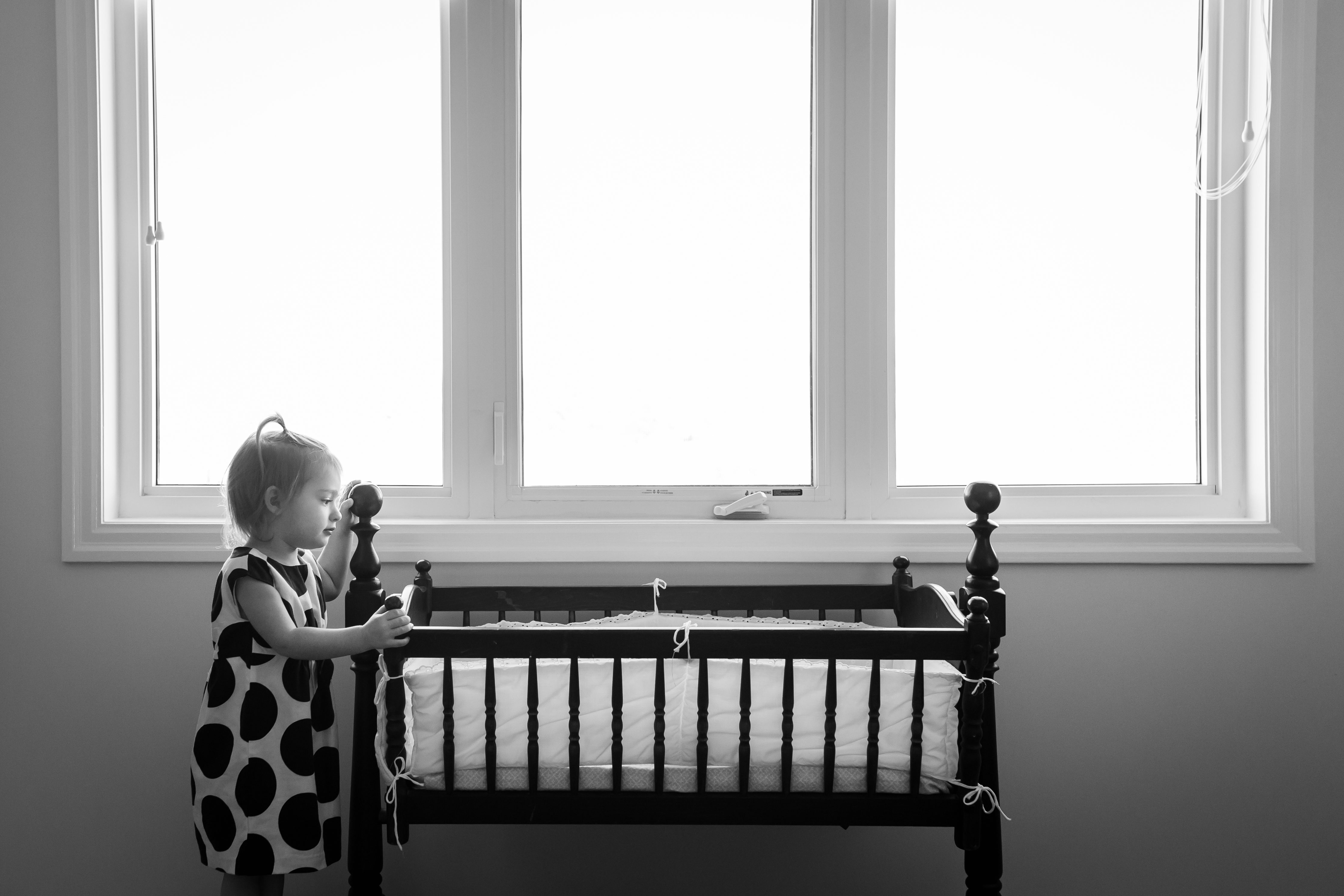 big sister admiring her new baby sister in her antique bassinet
