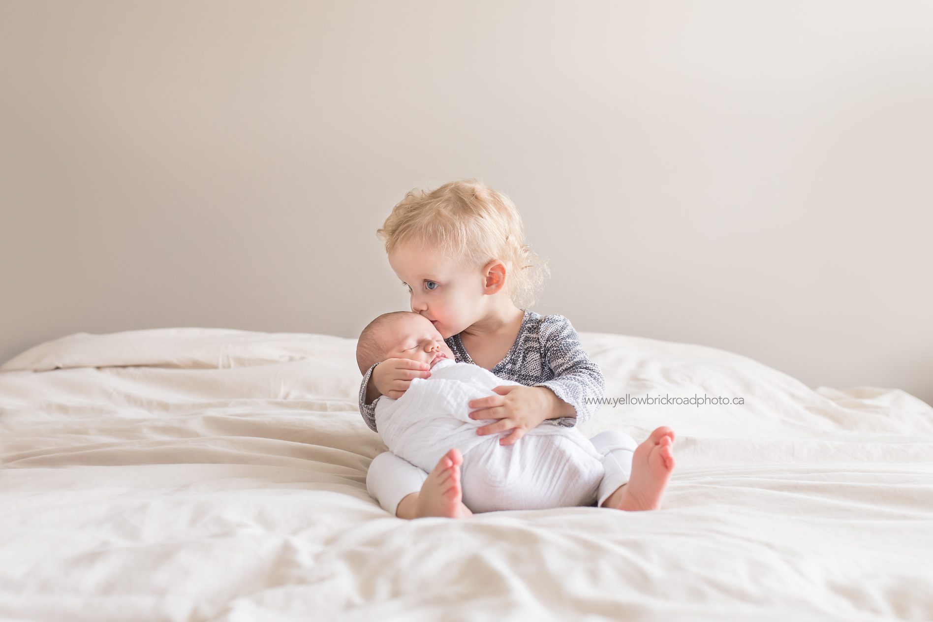 Lifestyle Newborn session sister holding newborn on bed www.yellowbrickroadphoto.ca